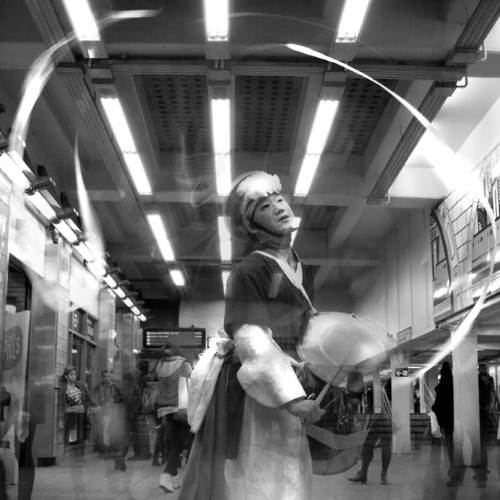 Korean man in traditional attire with traditional drum in hand performs in a NYC subway station